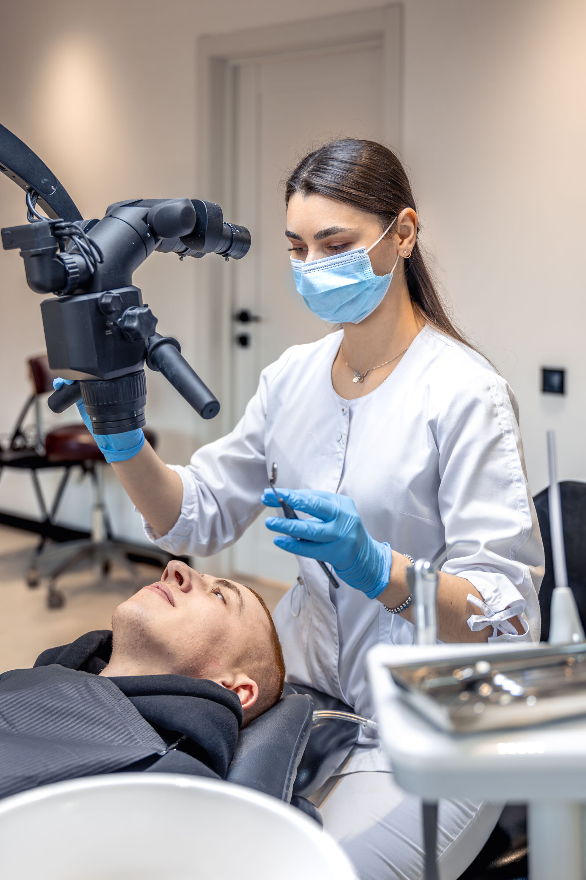 Young female dentist treating patient's teeth with dental microscope.